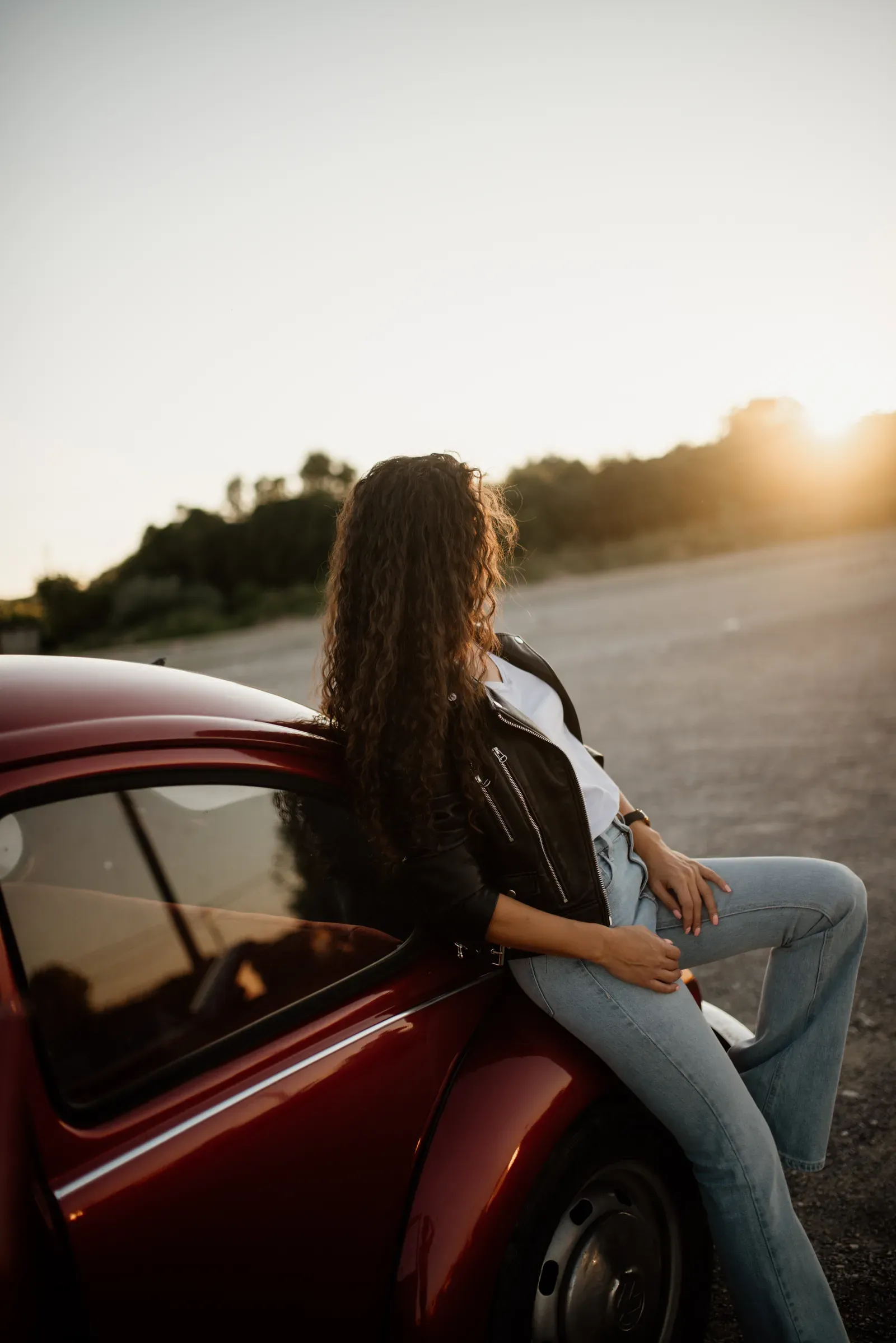 Gen Z Is Falling in Love With Classic Cars (Young woman with curly hair standing besides a classic car with sunset background., CC BY 2.0)